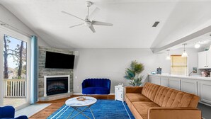 Ein modernes Wohnzimmer mit Kamin, einem blauen Sessel, einem braunen Sofa und einem Essbereich mit Küchenzeile.