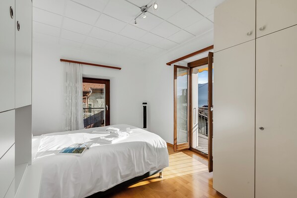 Un dormitorio con cama, armario, puerta corrediza de vidrio a un balcón y ventilador de techo.