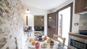 A dining area with a stone wall, a table set with plates, cups, and a variety of food items. There is a kitchen area with a stove and oven visible.