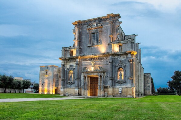 A historic church with a central entrance, flanked by two smaller wings, set against a twilight sky.