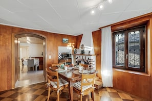 Un coin repas avec une table et des chaises en bois, une cuisine à l’arrière-plan et une fenêtre avec des rideaux.