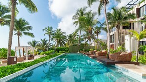 A swimming pool with clear blue water, surrounded by palm trees and lounge chairs. - OCEANFRONT LUXURY CONDO IN TULUM/TANKAH WITH BEACHCLUB (Tulum)