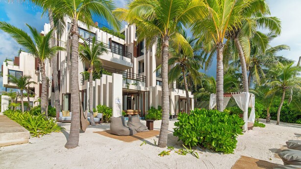 A modern resort with a two-story building, palm trees, and a sandy beach. - OCEANFRONT LUXURY CONDO IN TULUM/TANKAH WITH BEACHCLUB (Tulum)