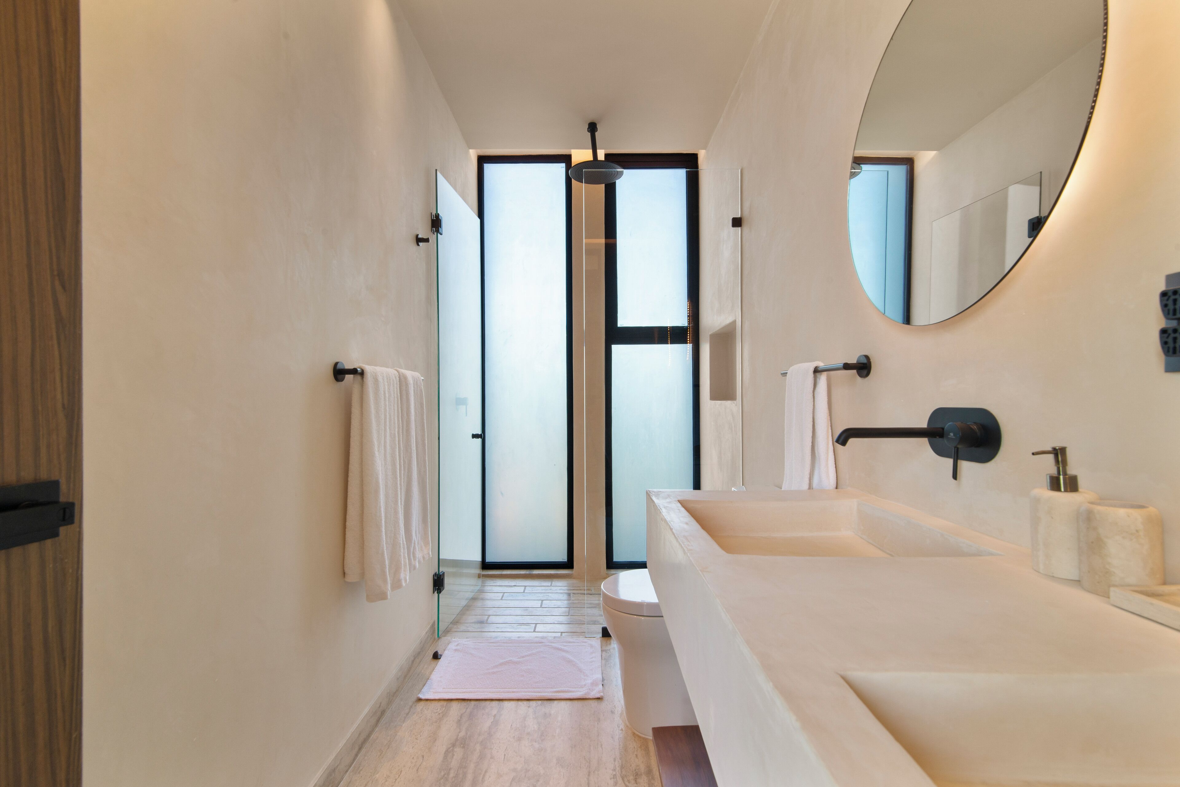 A modern bathroom with a large mirror, two sinks, and a glass shower door.