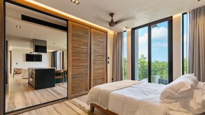 A modern bedroom with a large bed, a sliding door leading to a bathroom, and a view of greenery outside. - OCEANFRONT LUXURY CONDO IN TULUM/TANKAH WITH BEACHCLUB (Tulum)