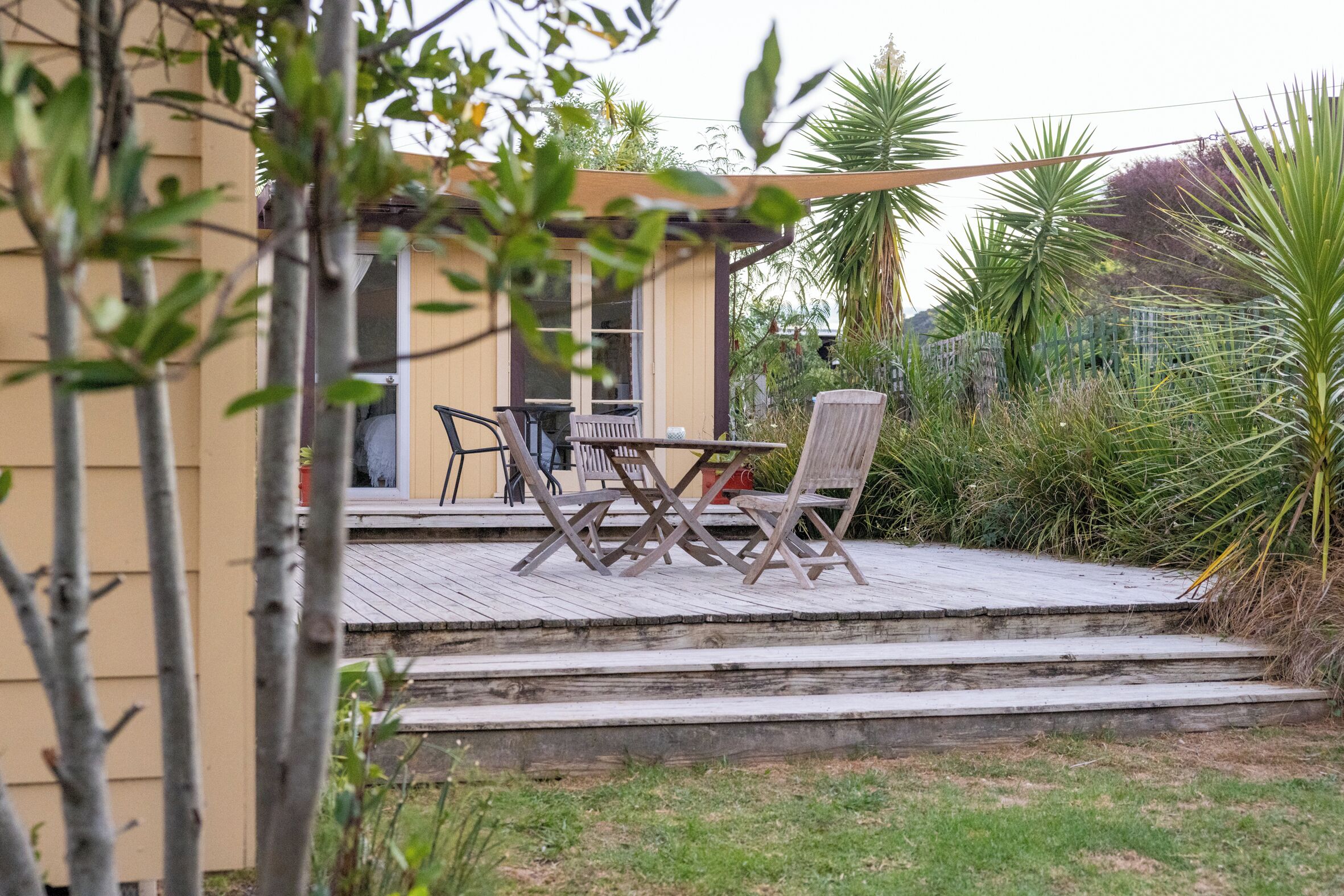 A patio with a wooden table and chairs, a small deck, and a house in the background.