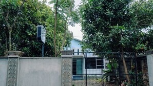 Un área cercada con un muro de concreto y una reja metálica, un cartel y un edificio al fondo.