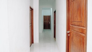 Un pasillo con paredes blancas y piso de baldosas, que lleva a una puerta de madera al final.