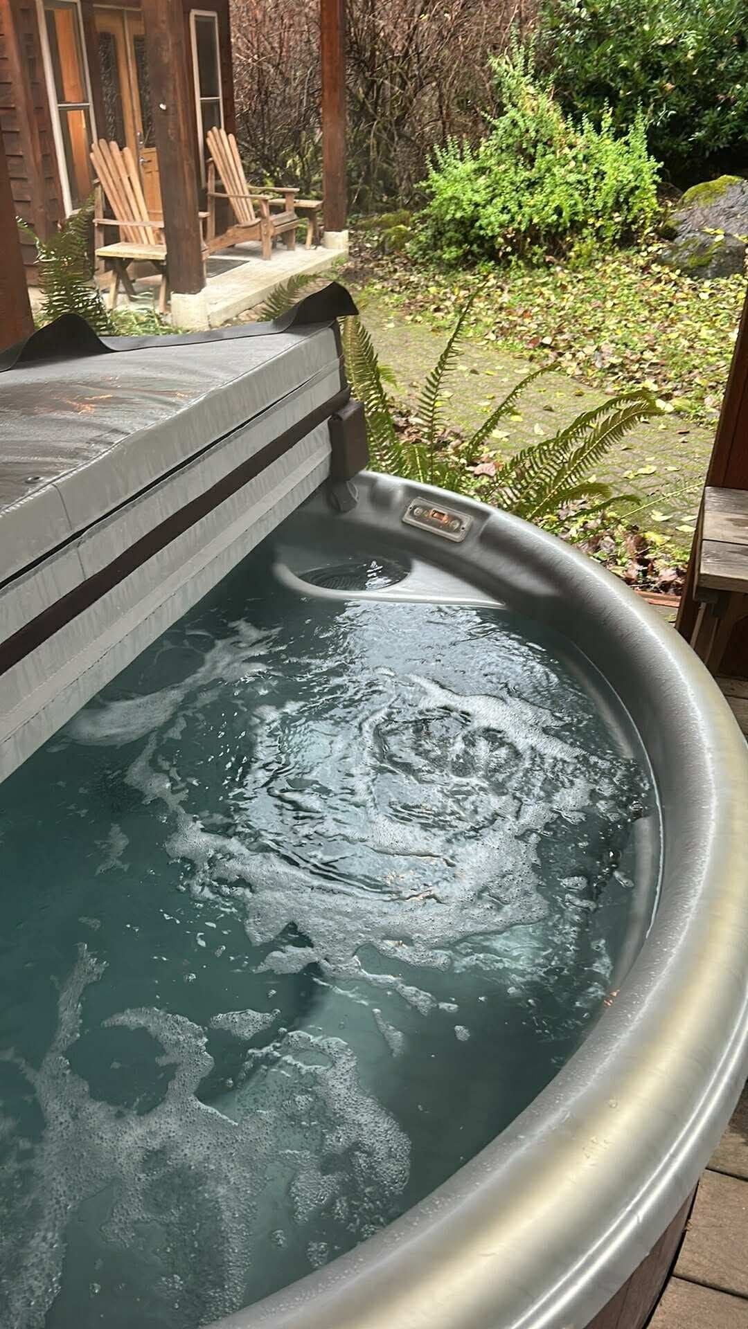 A hot tub with water, surrounded by a wooden deck and greenery.