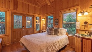 A wooden room with a bed, a window, a sink, and a door.