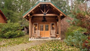 A wooden cabin with a porch, two windows, and a door.