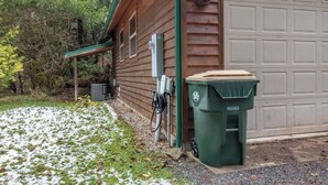 A wooden building with a garage door, a green trash bin, and electrical boxes.