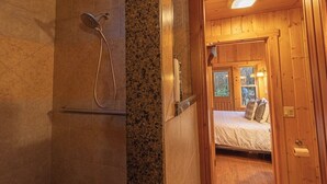 A wooden cabin interior with a shower, a bed, and a window.