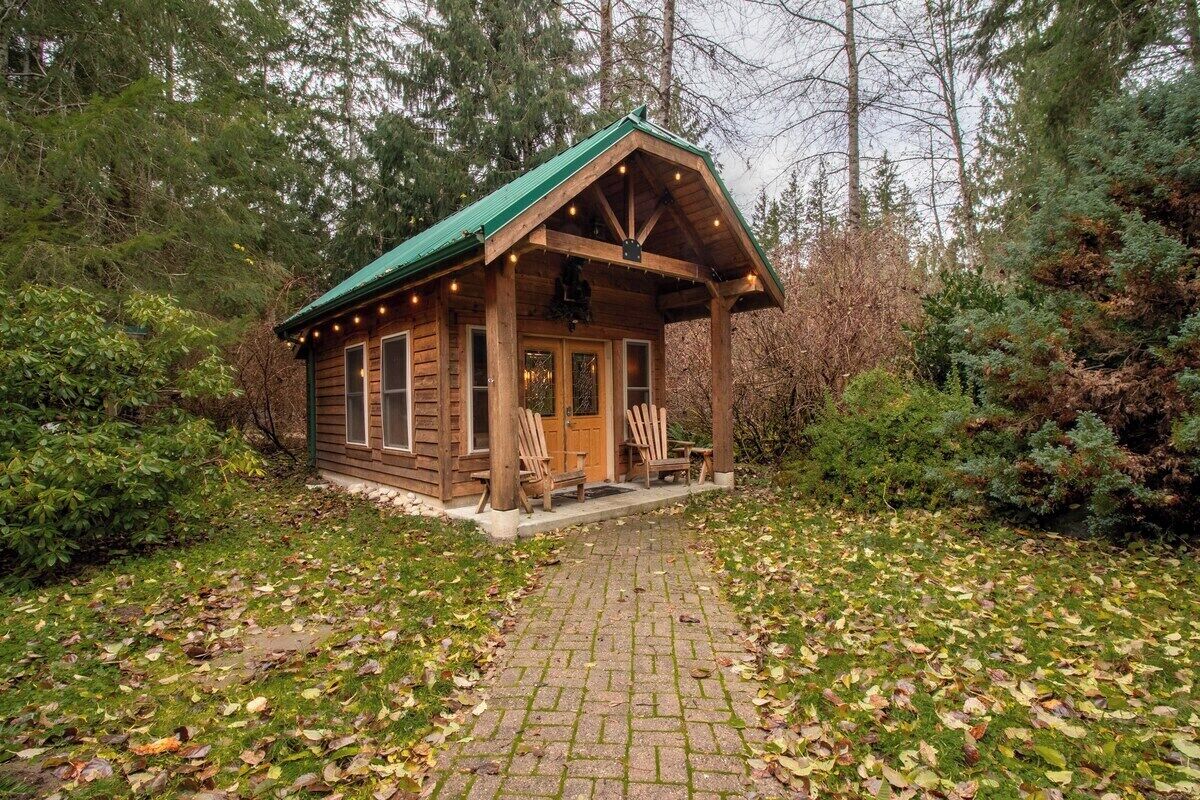 A rustic cabin with a porch, wooden exterior, and a green roof.