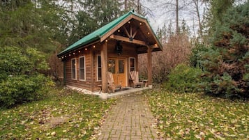 A rustic cabin with a porch, wooden exterior, and a green roof.