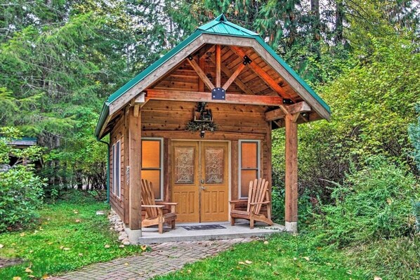 A wooden cabin with a green roof, two wooden chairs outside, and a brick pathway leading to it.