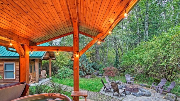 A wooden deck with a hot tub, outdoor seating, and a view of a forested area.