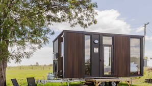 Une cabane moderne et compacte, dotée d’une grande porte coulissante, d’un petit espace porche et offrant une vue sur le paysage environnant.