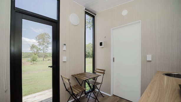Une cuisine moderne avec une table et des chaises en bois, une grande fenêtre et une porte donnant sur l’extérieur.