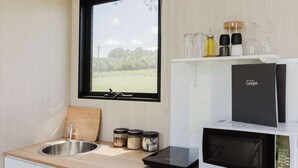 Une cuisine équipée d’un évier, d’un four à micro-ondes et d’une fenêtre donnant sur un espace verdoyant.