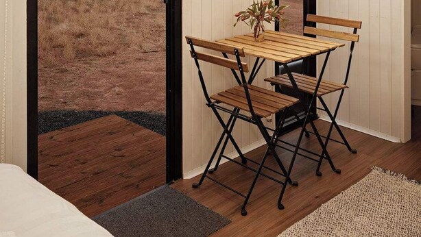 Une pièce avec une table et des chaises en bois, une grande fenêtre donnant sur un champ, et une porte menant à l’extérieur.