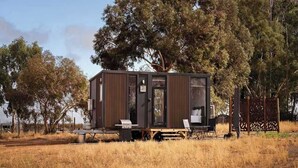 Une petite cabane moderne dotée d’une porte coulissante, d’une petite table et d’une chaise à l’extérieur.