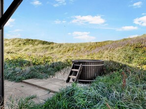 Un bain à remous en bois, avec une échelle en bois, situé dans un espace herbeux.