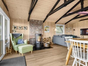 A cozy living room with a fireplace, a sofa, a dining table, and a TV. - 5 Star Holiday Home in Lokken (Lokken)