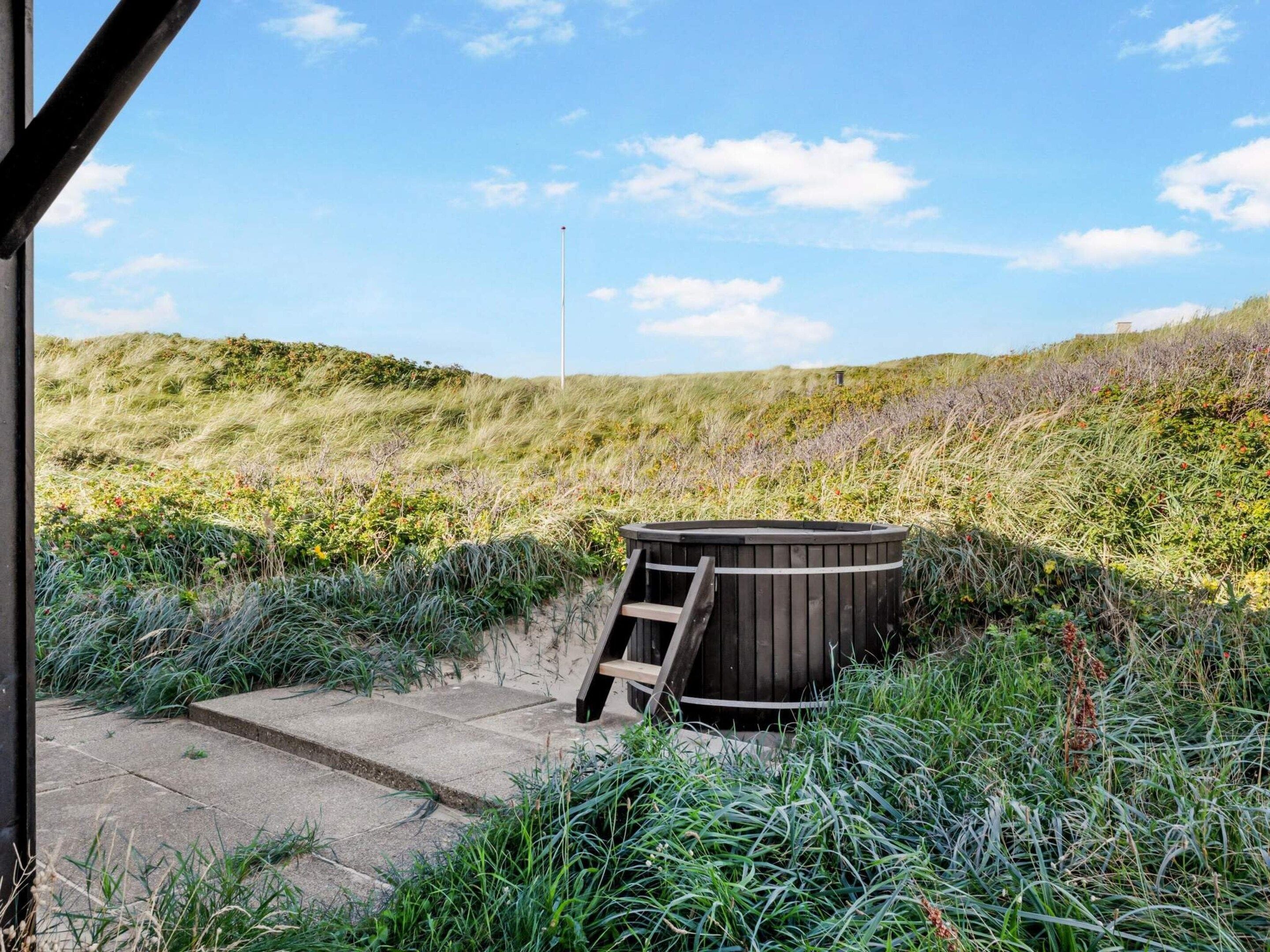Un bain à remous installé dans un cadre naturel, avec un chemin en béton menant à celui-ci.