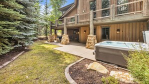 A wooden building with a covered patio, stone seating, and a hot tub.