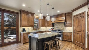 A spacious kitchen with wooden cabinets, a large island with stools, and pendant lighting.