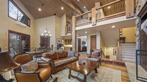 A spacious living area with a high ceiling, wooden beams, a large sofa, a coffee table, and a staircase leading to an upper level.