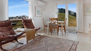 A spacious room with a large window, a dining area with wooden chairs and a table, and a brown leather sofa.