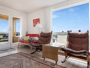 Une pièce spacieuse avec une grande fenêtre, un canapé rouge, des fauteuils en cuir marron, une table basse en bois et un tapis à motifs.