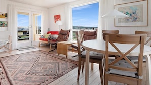 A spacious living room with a large window, a red sofa, a wooden dining table, and a patterned rug.