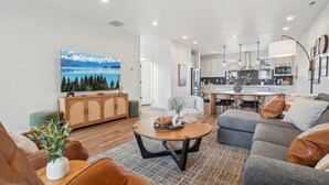 A modern living room with a large painting, a dining area, and a kitchen. - The Foxtrot at Mesa Arch Lane (Mountain Green)