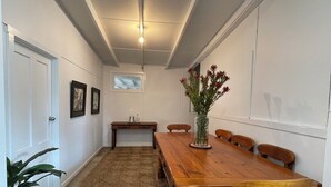 Un comedor con mesa de madera, sillas, un florero con flores, una mesita con una jarra y una alfombra.