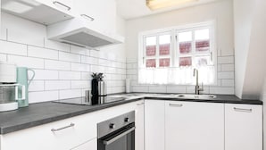 A modern kitchen with white cabinets, a black countertop, a built-in oven, and a window with a view of a red-roofed building. - 5 Star Holiday Home in Lokken (Lokken)