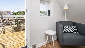 A modern living room with a grey sofa, a small white table, and a floor lamp. A wooden deck is visible outside the window. - 5 Star Holiday Home in Lokken (Lokken)