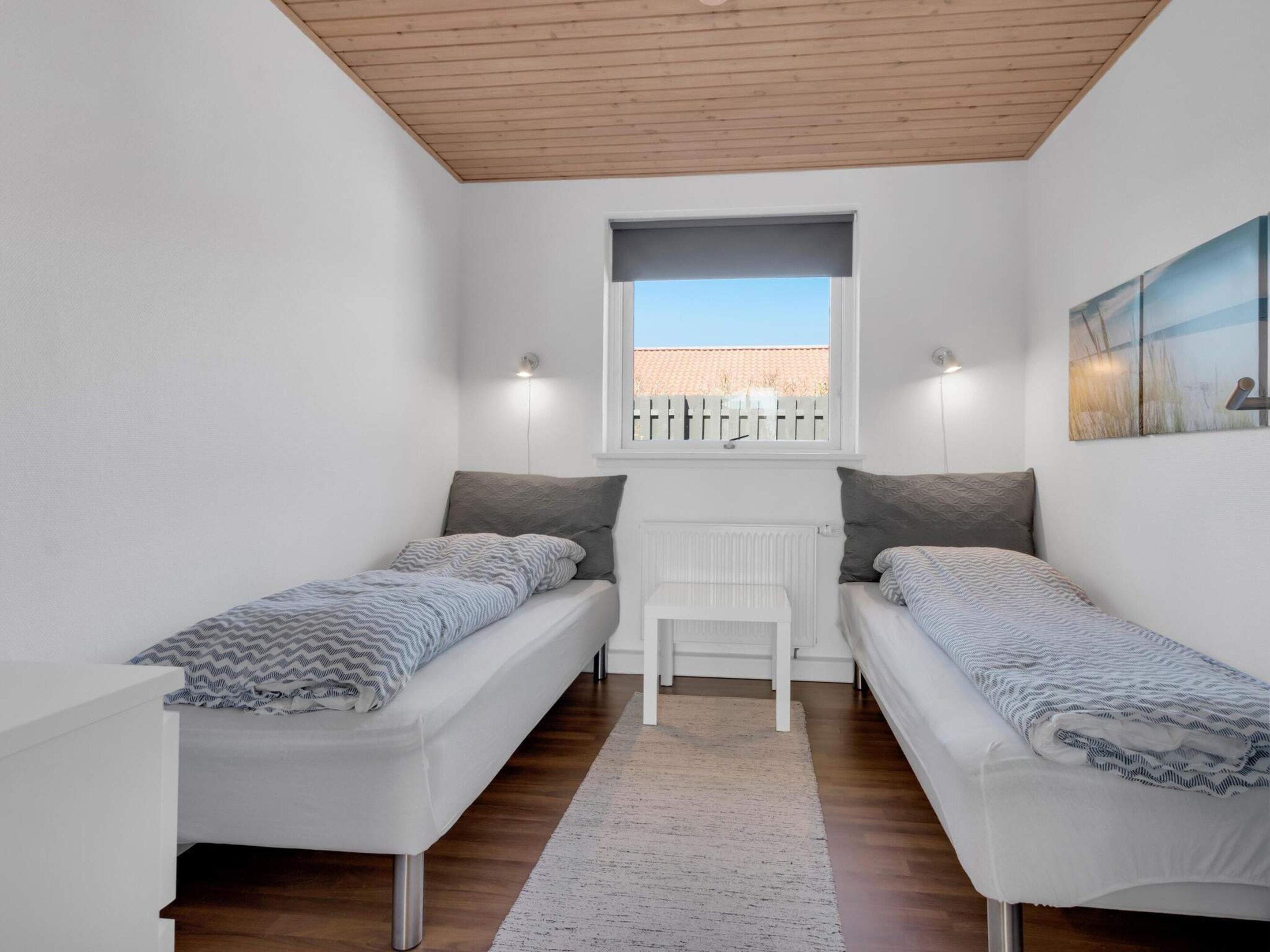 A small, modern room with two single beds, a white radiator, a window with a view, and a painting on the wall.