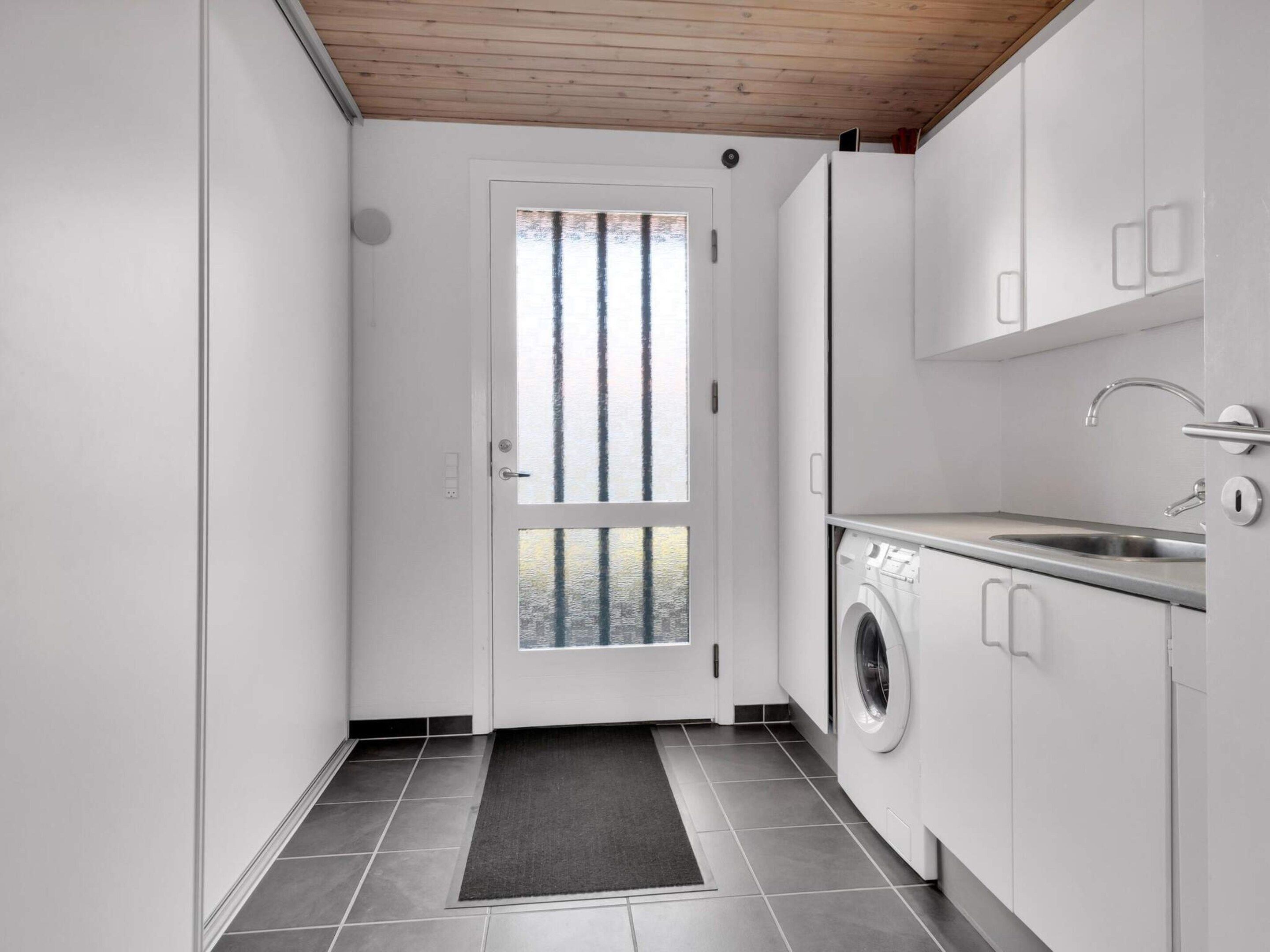 A compact laundry room with a washing machine, a sink, and a door with a view of trees.