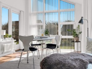 A bright, sunlit room with a dining table, chairs, and a large window with blinds. - 5 Star Holiday Home in Lokken (Lokken)