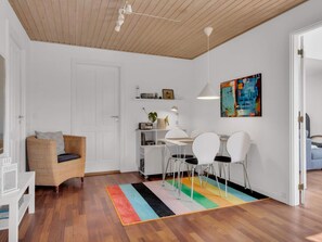 A modern living room with a dining area, white walls, wooden flooring, and a colorful rug. - 5 Star Holiday Home in Lokken (Lokken)