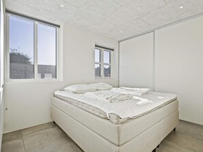 A bedroom with a bed, two windows, and a view of the outside.