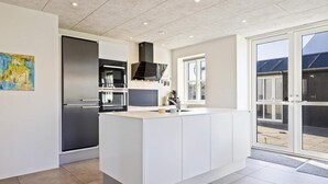 A modern kitchen with a central island, built-in ovens, and a large window. - 5 Star Holiday Home in Lokken (Lokken)
