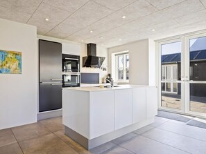 A modern kitchen with a large island, built-in appliances, and a sliding glass door leading to an outdoor area. - 5 Star Holiday Home in Lokken (Lokken)