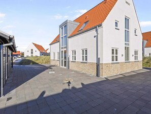 Un bâtiment moderne doté d’un toit en pente, de grandes fenêtres et d’un espace d’entrée pavé.
