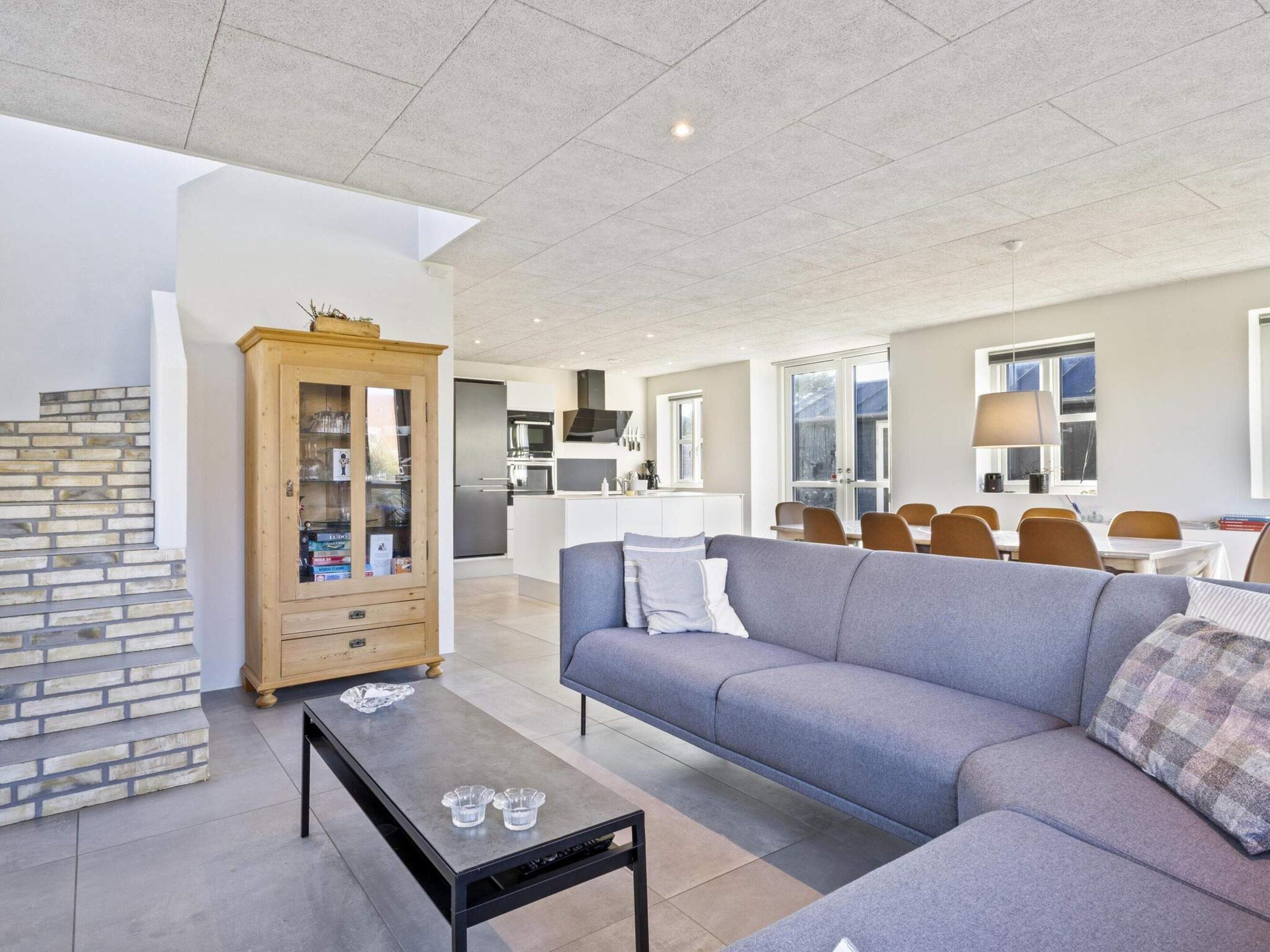 Una sala de estar moderna con un sofá gris, un mueble de madera y un comedor con sillas y una mesa.