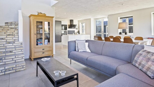 A modern living room with a grey sofa, a wooden cabinet, and a dining area with a table and chairs. - 5 Star Holiday Home in Lokken (Lokken)