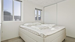 A bedroom with a large bed, two windows, and a view of the outside. - 5 Star Holiday Home in Lokken (Lokken)